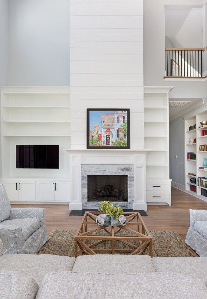 Inspiration for a mid-sized beach style open concept family room in Charleston with a home bar, grey walls, medium hardwood floors, a standard fireplace, a stone fireplace surround, a built-in media wall and brown floor.