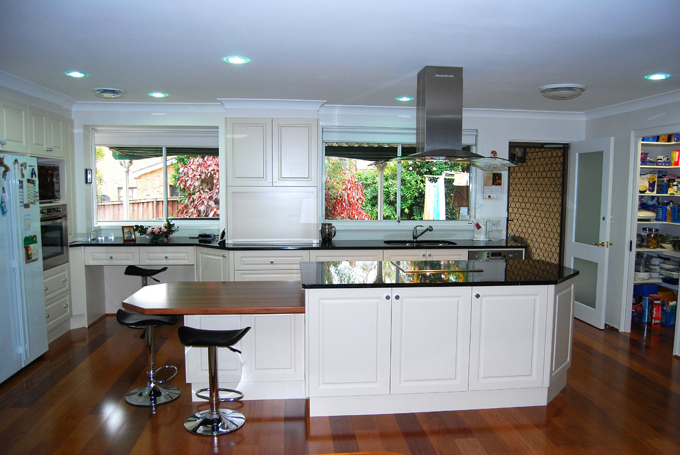 Inspiration for a large transitional l-shaped kitchen pantry in Sydney with an undermount sink, recessed-panel cabinets, white cabinets, granite benchtops, grey splashback, glass sheet splashback, stainless steel appliances, medium hardwood floors and with island.