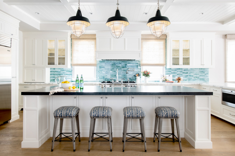 This is an example of a large beach style u-shaped eat-in kitchen in Los Angeles with a farmhouse sink, recessed-panel cabinets, white cabinets, soapstone benchtops, blue splashback, ceramic splashback, stainless steel appliances, light hardwood floors, with island, beige floor, black benchtop and coffered.