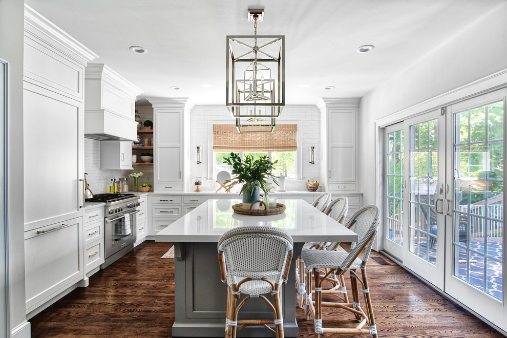 Photo of a traditional l-shaped kitchen in New York with quartz benchtops, shaker cabinets, white cabinets, white splashback, subway tile splashback, panelled appliances, dark hardwood floors, with island, brown floor and white benchtop.