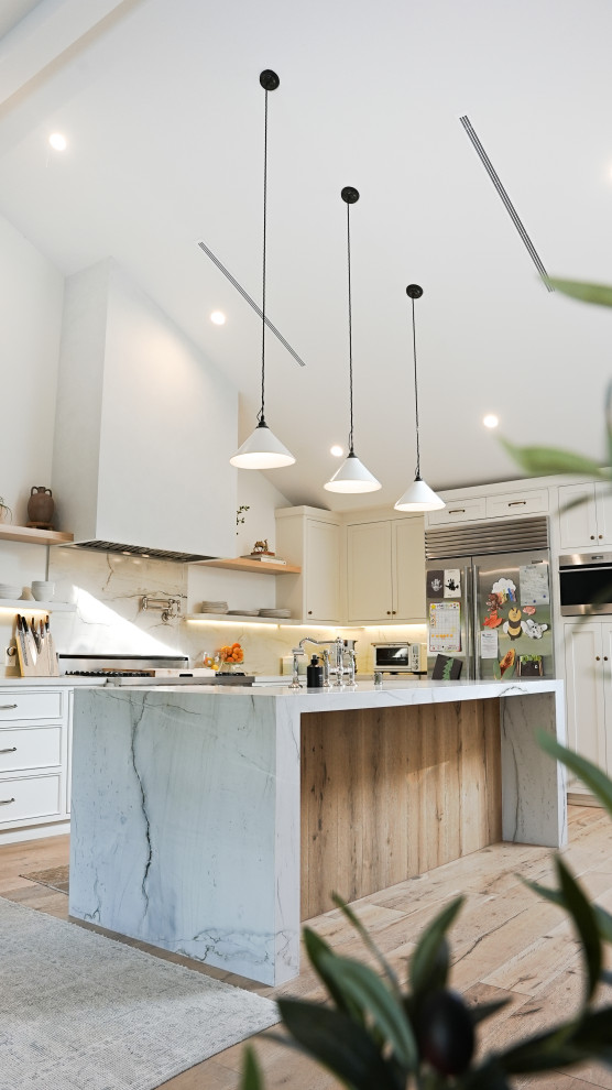 Large scandinavian l-shaped eat-in kitchen in Los Angeles with a farmhouse sink, beaded inset cabinets, white cabinets, quartzite benchtops, white splashback, stone slab splashback, stainless steel appliances, light hardwood floors, with island, beige floor, white benchtop and vaulted.