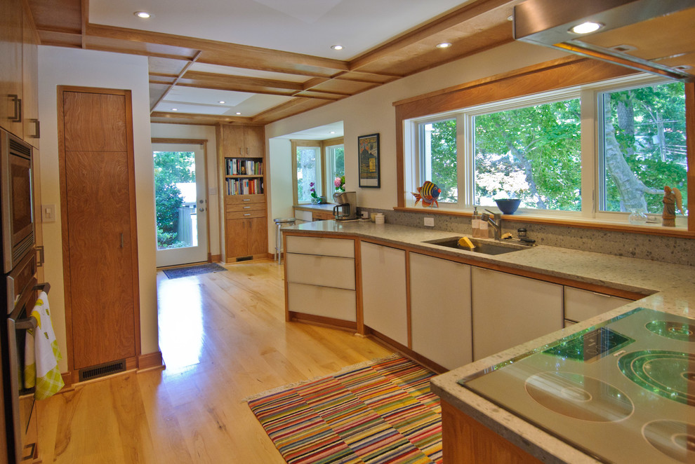 Example of a transitional u-shaped enclosed kitchen design in DC Metro with an undermount sink, flat-panel cabinets, light wood cabinets, solid surface countertops, orange backsplash, glass sheet backsplash and stainless steel appliances