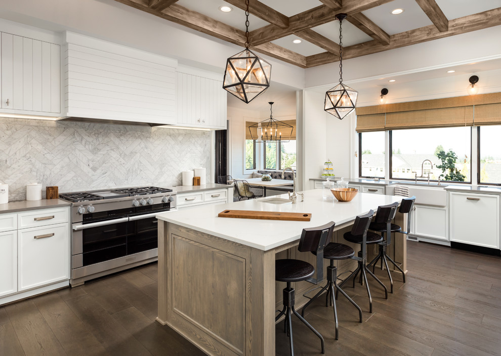 Inspiration for a country l-shaped eat-in kitchen in Los Angeles with a farmhouse sink, white cabinets, white splashback, stainless steel appliances, medium hardwood floors, with island, brown floor and white benchtop.