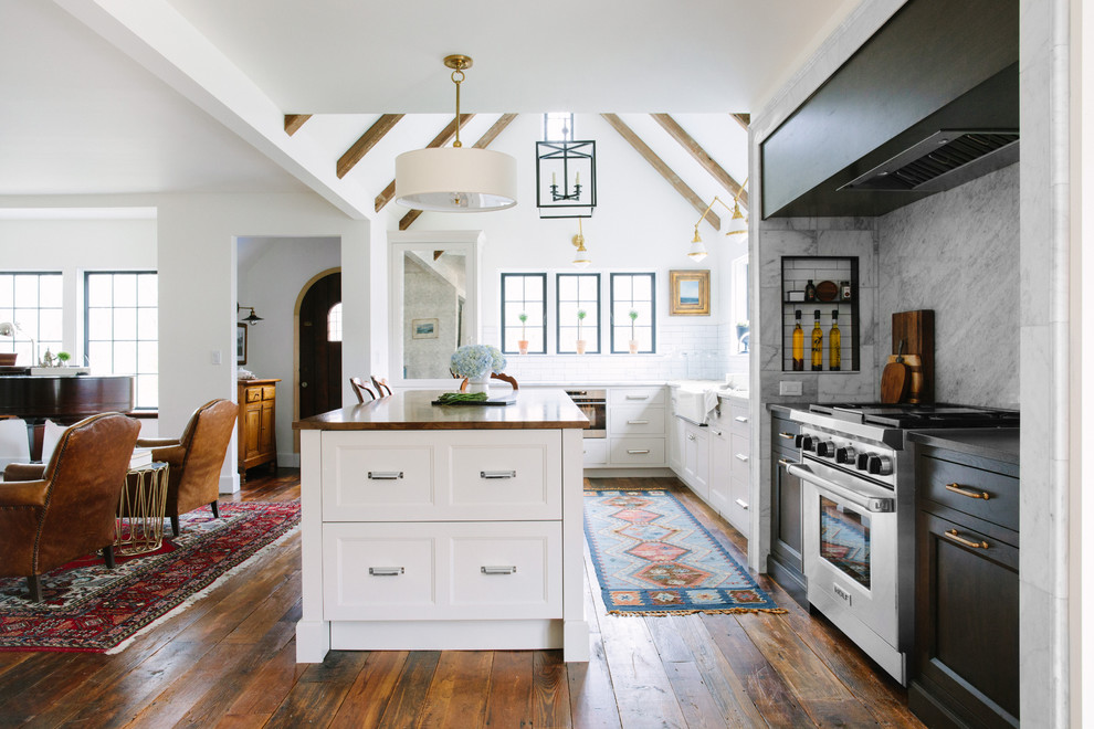 Photo of a mid-sized country l-shaped open plan kitchen in Grand Rapids with a farmhouse sink, recessed-panel cabinets, white splashback, subway tile splashback, with island, white cabinets, stainless steel appliances, wood benchtops and dark hardwood floors.