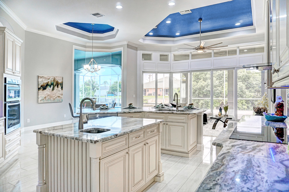 Photo of a mediterranean kitchen in Miami with an undermount sink, raised-panel cabinets, beige cabinets, stainless steel appliances, multiple islands, multi-coloured benchtop and white floor.