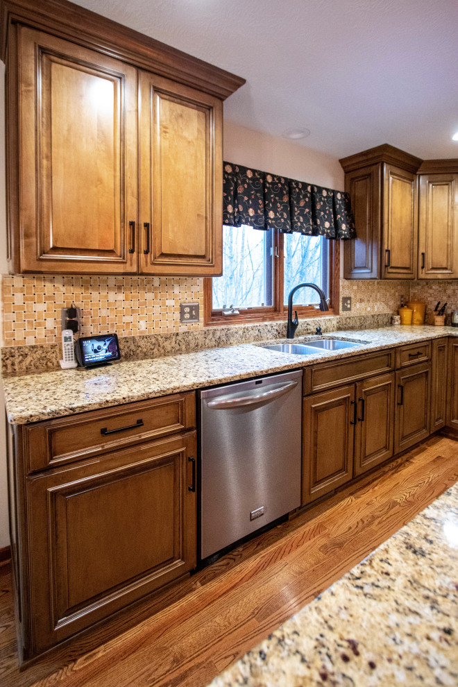 This is an example of a mid-sized traditional galley eat-in kitchen in Cleveland with an undermount sink, raised-panel cabinets, granite benchtops, beige splashback, porcelain splashback, stainless steel appliances, medium hardwood floors, with island, brown floor and beige benchtop.