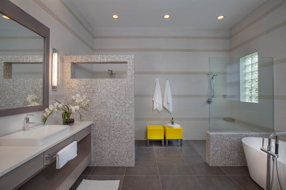 This is an example of a large contemporary master bathroom in Orlando with flat-panel cabinets, grey cabinets, a freestanding tub, an open shower, gray tile, beige walls, porcelain floors, a vessel sink, engineered quartz benchtops and mosaic tile.