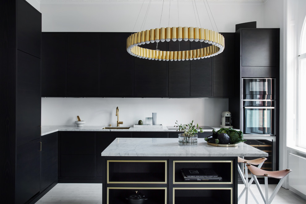 Inspiration for an expansive contemporary l-shaped open plan kitchen in Malmo with a single-bowl sink, flat-panel cabinets, marble benchtops, white splashback, stainless steel appliances, light hardwood floors, with island and black cabinets.