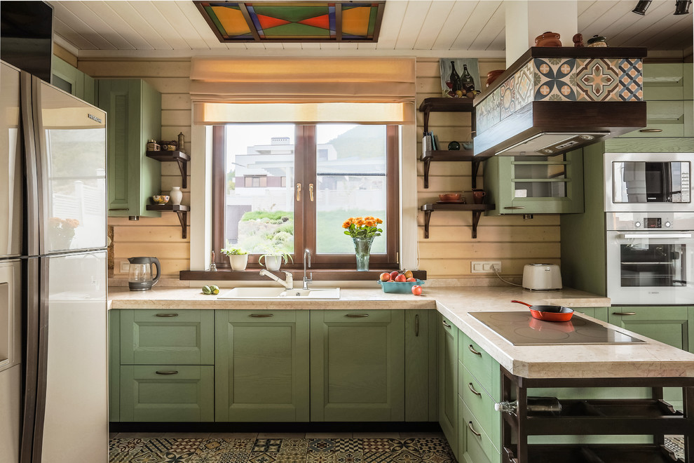 This is an example of a country u-shaped kitchen in Other with a drop-in sink, green cabinets, beige splashback, white appliances, a peninsula, multi-coloured floor, recessed-panel cabinets, timber splashback and cement tiles.