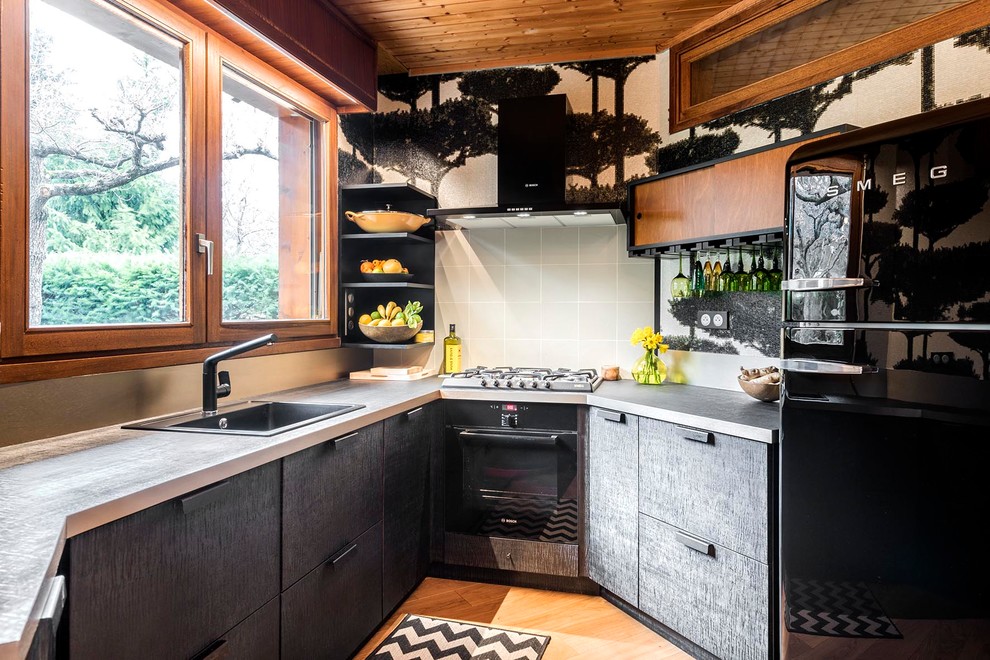 This is an example of a small contemporary kitchen in Clermont-Ferrand with black cabinets, laminate benchtops, a drop-in sink, flat-panel cabinets, grey splashback, black appliances, medium hardwood floors and orange floor.