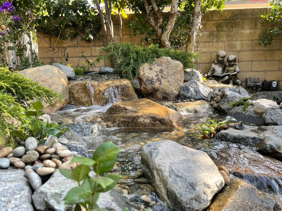Ejemplo de jardín tropical de tamaño medio en primavera en patio trasero con fuente, estanque, exposición parcial al sol y piedra decorativa