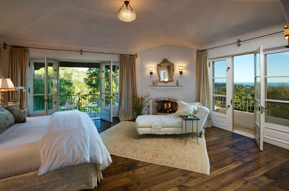 This is an example of a mediterranean master bedroom in Santa Barbara with dark hardwood floors, a corner fireplace and a brick fireplace surround.