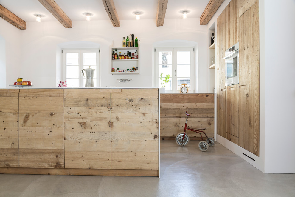This is an example of a large industrial galley open plan kitchen in Munich with an undermount sink, flat-panel cabinets, light wood cabinets, solid surface benchtops, concrete floors and with island.