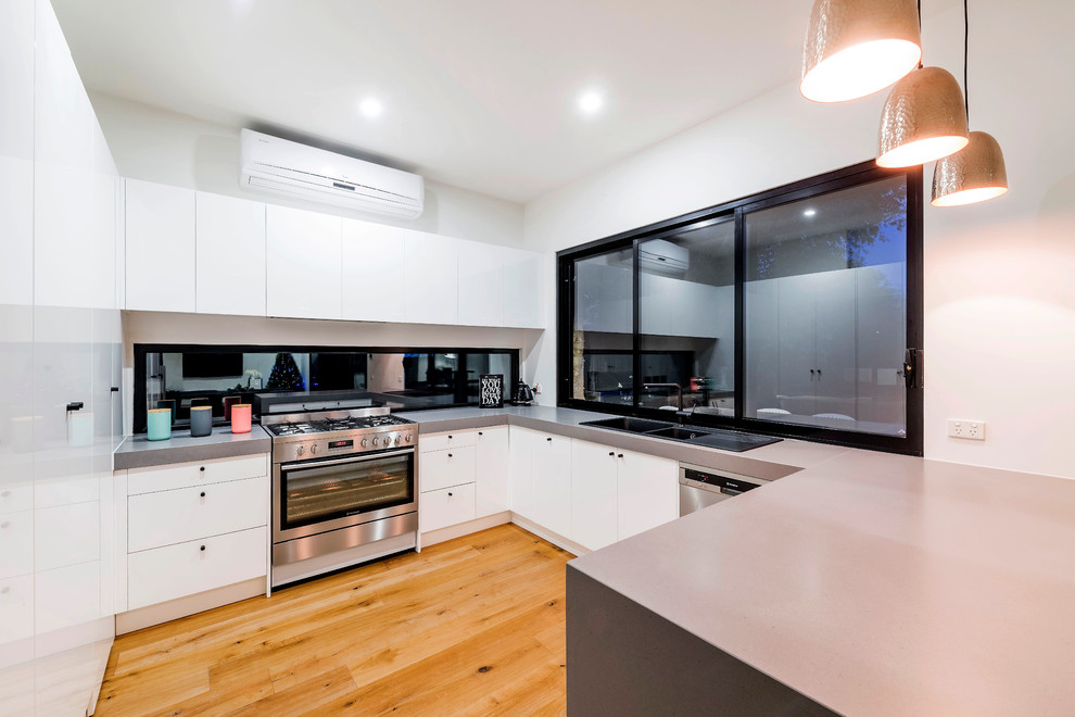 Inspiration for a mid-sized modern u-shaped kitchen in Melbourne with a double-bowl sink, white cabinets, stainless steel appliances, medium hardwood floors, no island, quartz benchtops and glass sheet splashback.