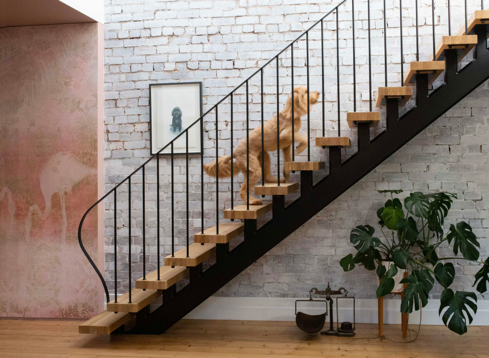 Inspiration pour un escalier sans contremarche droit design avec des marches en bois, un garde-corps en métal et un mur en parement de brique.