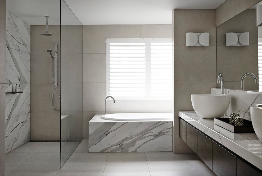 Photo of a large modern bathroom in Melbourne with a vessel sink, flat-panel cabinets, dark wood cabinets, marble benchtops, a drop-in tub, a curbless shower and marble.