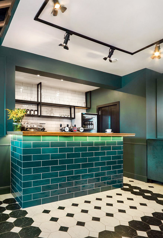 Photo of a small transitional single-wall seated home bar in Yekaterinburg with shaker cabinets, blue cabinets, wood benchtops, white splashback, ceramic splashback, marble floors, multi-coloured floor and brown benchtop.