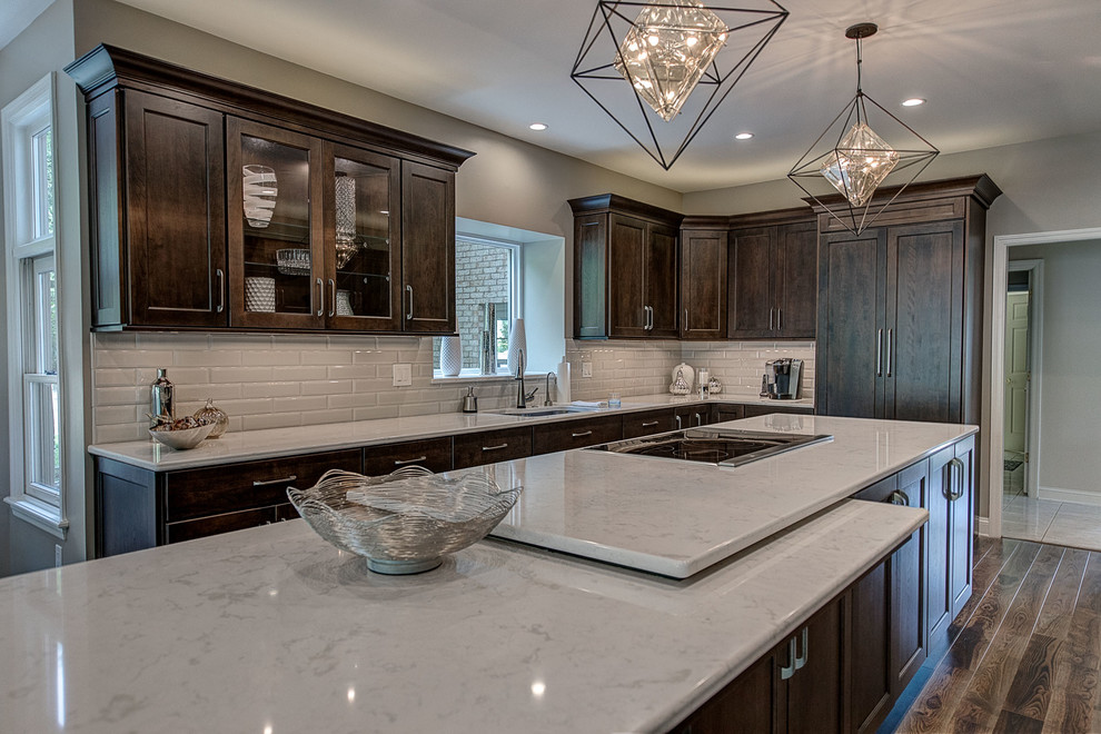 Eat-in kitchen - large transitional l-shaped brown floor and medium tone wood floor eat-in kitchen idea with an undermount sink, flat-panel cabinets, dark wood cabinets, white backsplash, an island, marble countertops, ceramic backsplash, stainless steel appliances and white countertops