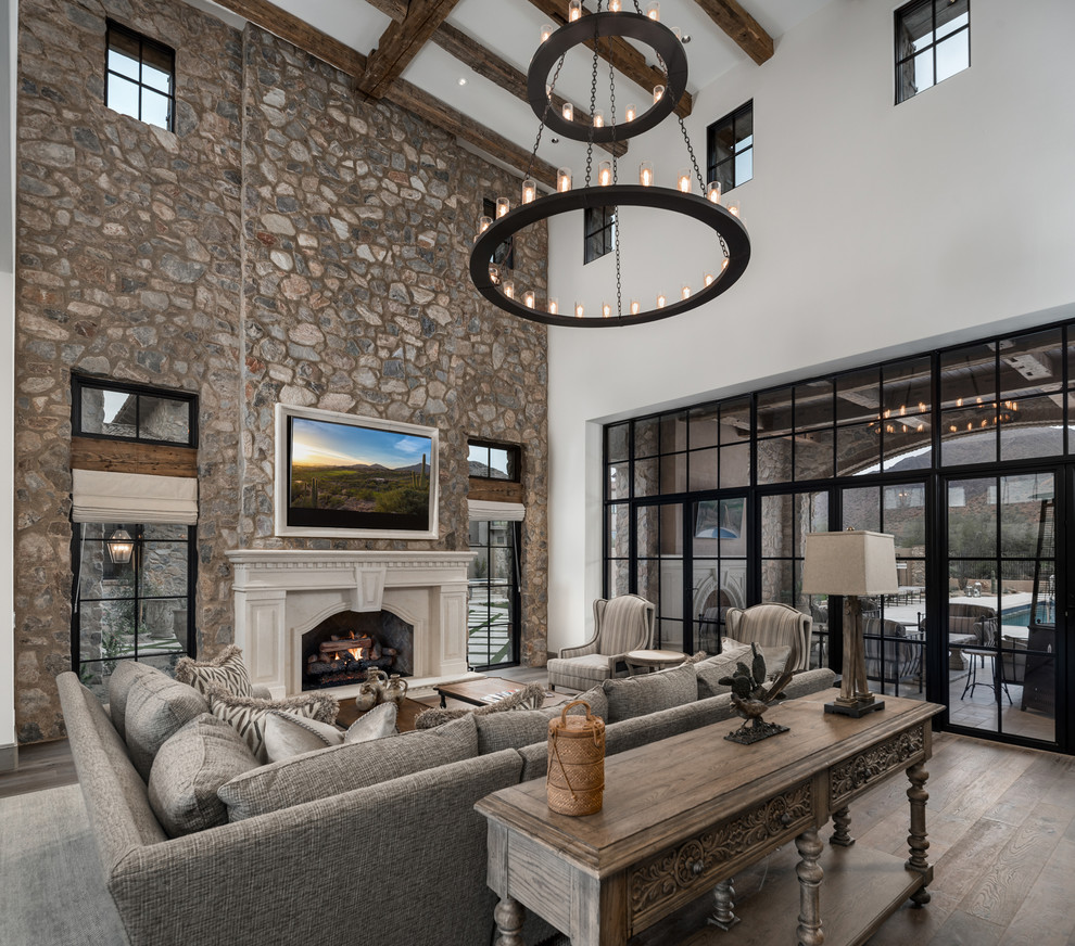 Expansive mediterranean formal open concept living room in Phoenix with multi-coloured walls, medium hardwood floors, a standard fireplace, a stone fireplace surround, a wall-mounted tv, multi-coloured floor and vaulted.