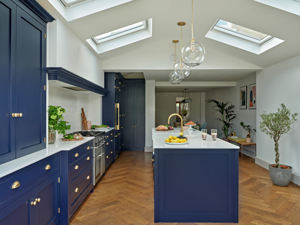 This is an example of a large transitional single-wall eat-in kitchen in London with shaker cabinets, with island, a farmhouse sink, blue cabinets, quartzite benchtops, white splashback, ceramic splashback, panelled appliances, white benchtop and vaulted.