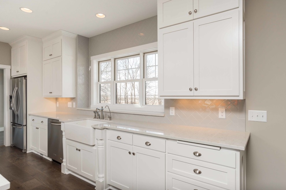 Inspiration for an expansive contemporary separate kitchen in Minneapolis with a farmhouse sink, shaker cabinets, white cabinets, white splashback, subway tile splashback, stainless steel appliances, dark hardwood floors and multiple islands.