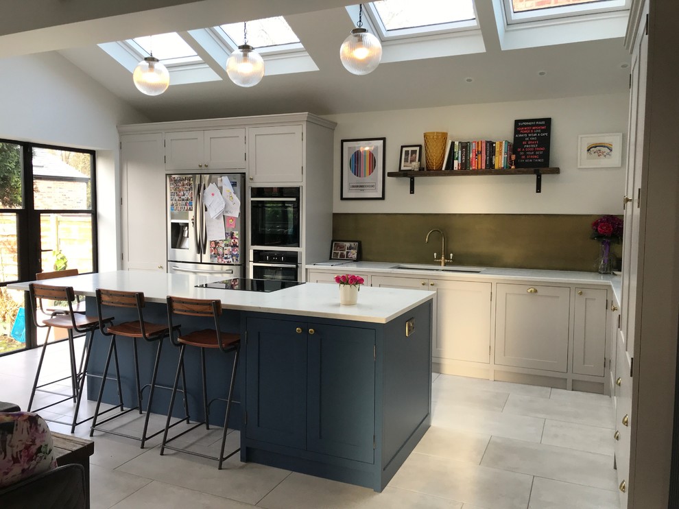 Design ideas for a mid-sized traditional l-shaped eat-in kitchen in Manchester with a drop-in sink, shaker cabinets, blue cabinets, quartzite benchtops, metallic splashback, panelled appliances, ceramic floors, with island, grey floor and white benchtop.