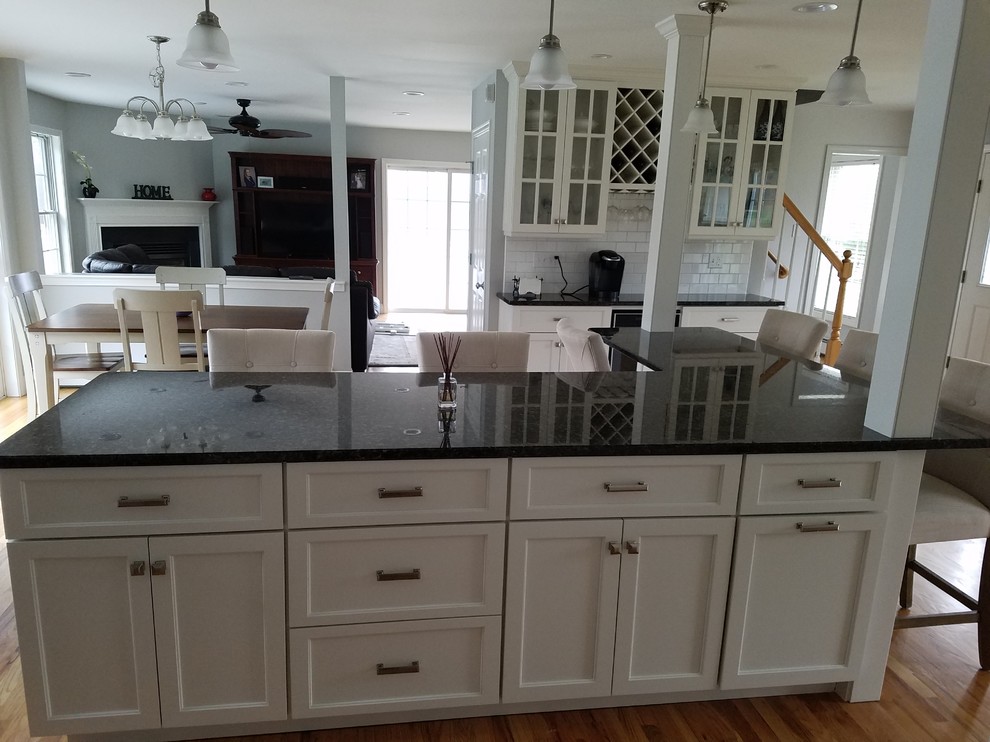 Inspiration for a large transitional l-shaped light wood floor and brown floor eat-in kitchen remodel with an undermount sink, shaker cabinets, white cabinets, granite countertops, white backsplash, subway tile backsplash, stainless steel appliances and an island