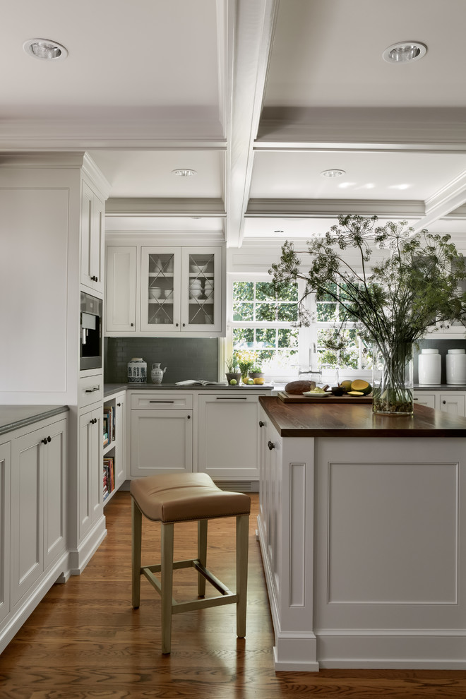 This is an example of a traditional kitchen in Portland with glass-front cabinets, white cabinets, grey splashback, medium hardwood floors and with island.