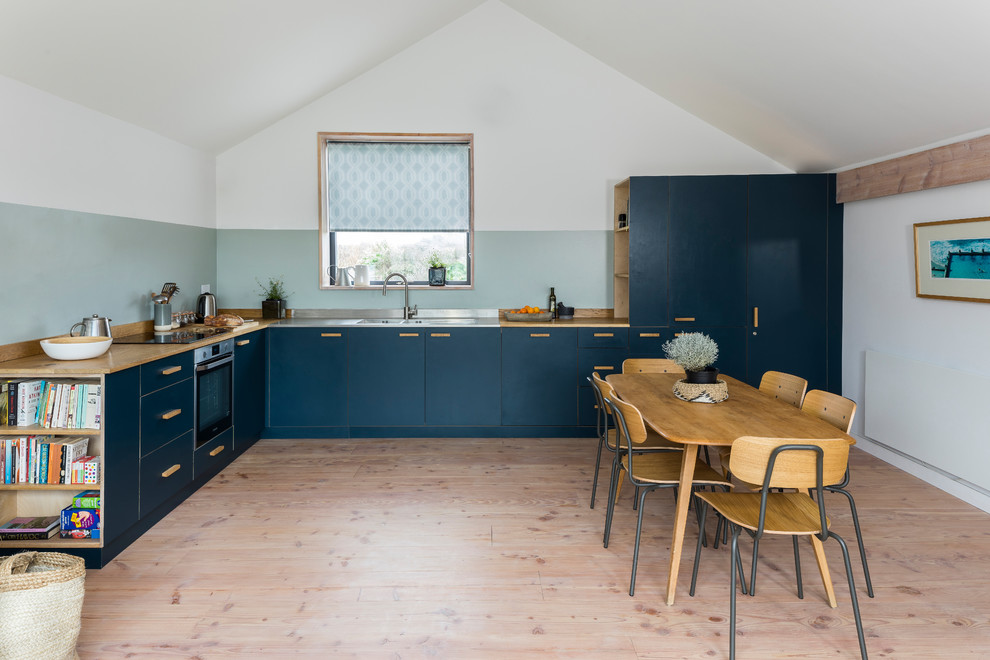 Inspiration for a mid-sized scandinavian l-shaped eat-in kitchen in London with a double-bowl sink, flat-panel cabinets, blue cabinets, light hardwood floors, no island, beige floor, wood benchtops, blue splashback and beige benchtop.