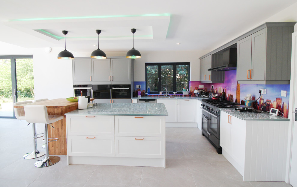 Design ideas for an expansive contemporary l-shaped open plan kitchen in London with an integrated sink, shaker cabinets, white cabinets, glass benchtops, multi-coloured splashback, glass tile splashback, black appliances, ceramic floors, with island, green benchtop and grey floor.
