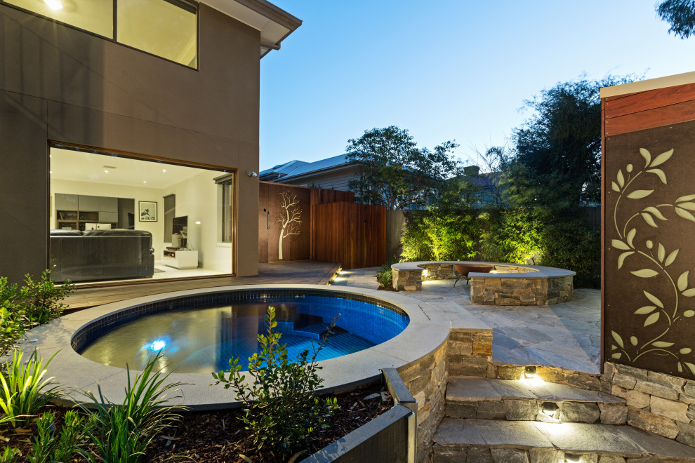This is an example of a large modern backyard round lap pool in Melbourne with a hot tub and decking.