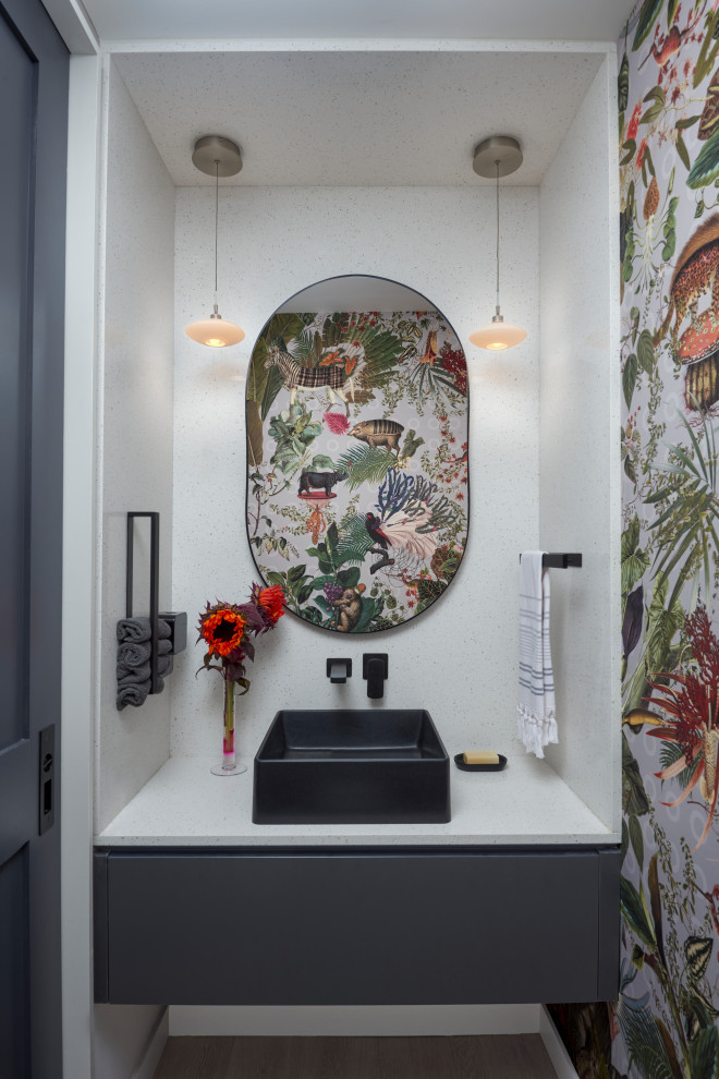 На фото: туалет в современном стиле с плоскими фасадами, серыми фасадами, разноцветными стенами, настольной раковиной, белой столешницей, подвесной тумбой и обоями на стенах с