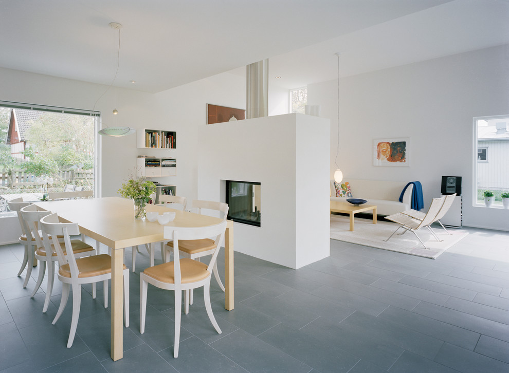 This is an example of a mid-sized scandinavian open plan dining in Malmo with white walls, ceramic floors, a two-sided fireplace and a concrete fireplace surround.