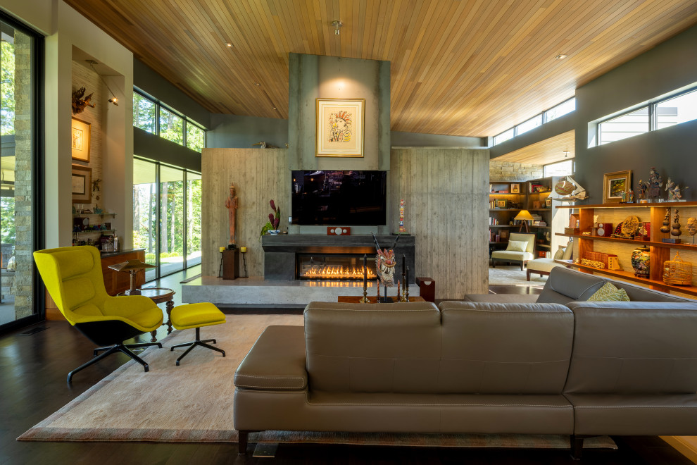 Photo of a mid-sized open concept living room in Seattle with a library, grey walls, dark hardwood floors, a two-sided fireplace, a concrete fireplace surround, a wall-mounted tv, brown floor and wood.