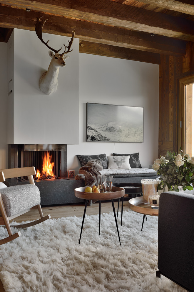 Modelo de salón abierto y gris y blanco actual grande con suelo de madera clara, chimenea de esquina, televisor colgado en la pared, vigas vistas, madera y paredes blancas