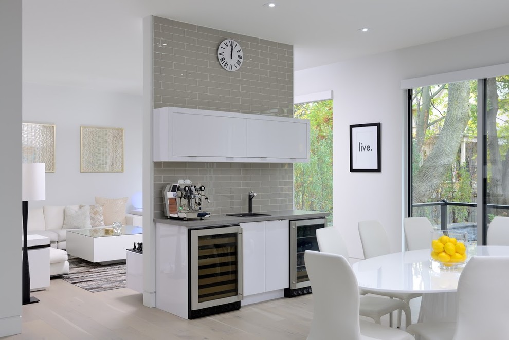 Mid-sized contemporary single-wall wet bar in Toronto with flat-panel cabinets, white cabinets, grey splashback, subway tile splashback, beige floor, a drop-in sink and light hardwood floors.