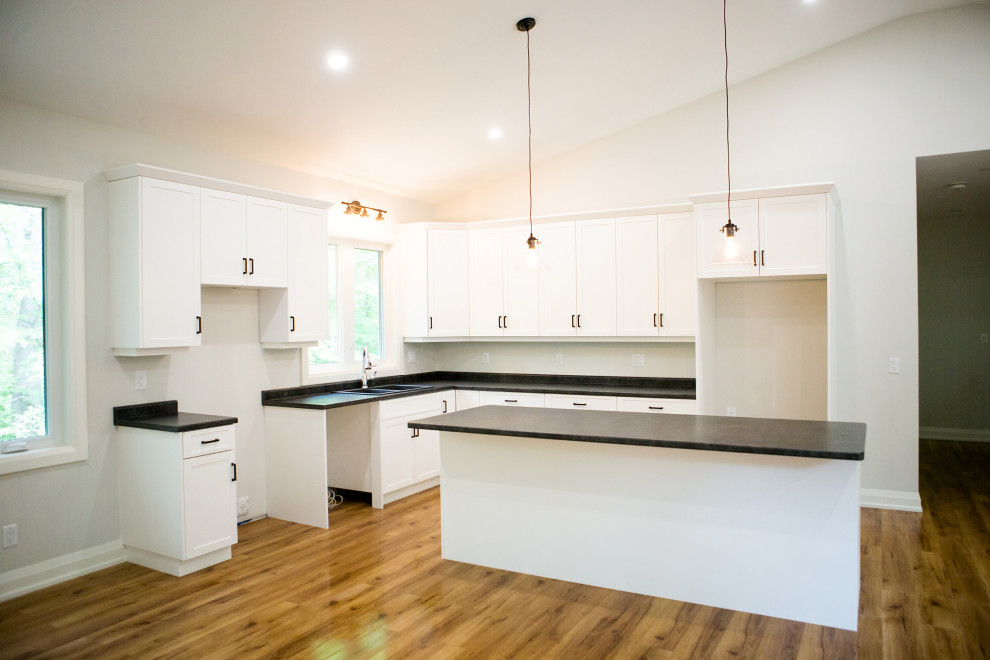 Mid-sized trendy l-shaped light wood floor, brown floor and vaulted ceiling eat-in kitchen photo in Toronto with a double-bowl sink, shaker cabinets, white cabinets, laminate countertops, an island and black countertops