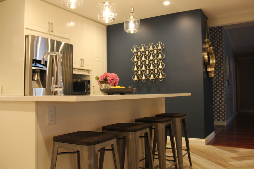 Open concept kitchen - large transitional l-shaped vinyl floor and brown floor open concept kitchen idea with an undermount sink, recessed-panel cabinets, white cabinets, quartz countertops, white backsplash, ceramic backsplash, stainless steel appliances and an island
