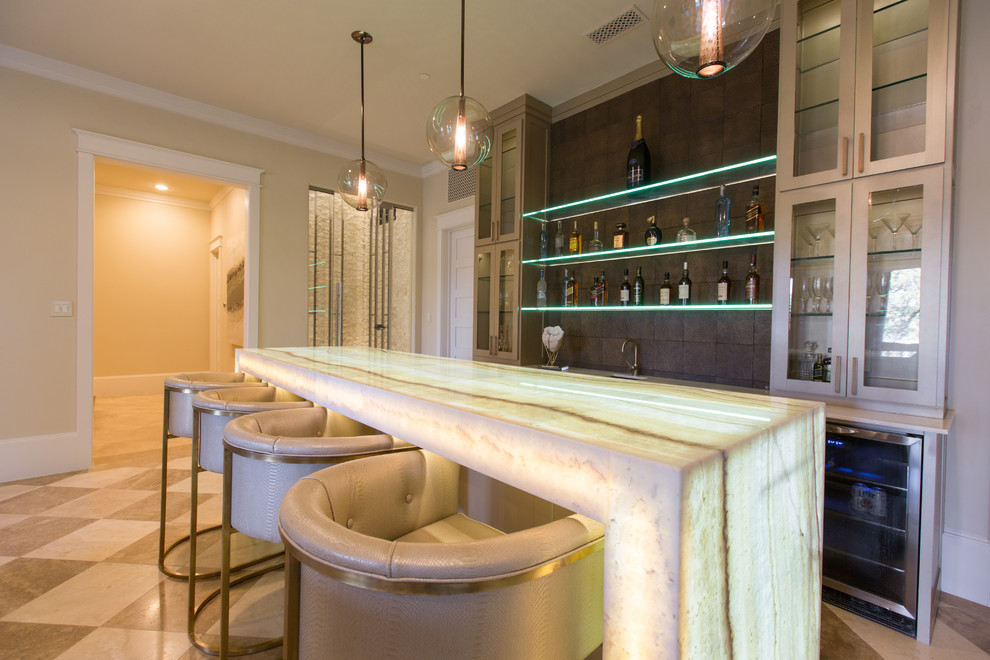 This is an example of a large contemporary single-wall seated home bar in Dallas with an undermount sink, glass-front cabinets, beige cabinets, onyx benchtops, brown splashback and white benchtop.
