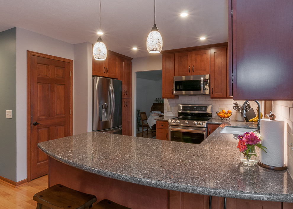 Photo of a mid-sized transitional u-shaped eat-in kitchen in Minneapolis with an undermount sink, shaker cabinets, medium wood cabinets, quartz benchtops, beige splashback, porcelain splashback, stainless steel appliances, light hardwood floors and a peninsula.