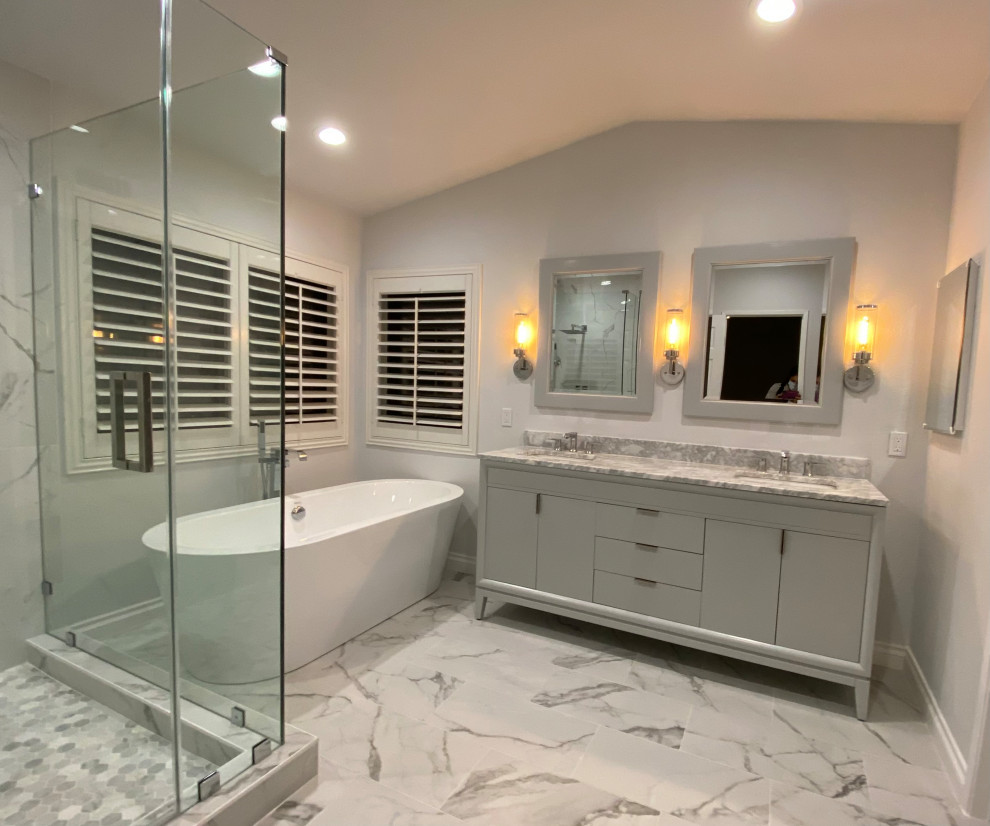 Cette image montre une salle de bain principale design de taille moyenne avec un placard à porte plane, des portes de placard grises, une baignoire indépendante, une douche d'angle, WC à poser, un carrelage gris, des carreaux de porcelaine, un mur gris, un sol en carrelage de porcelaine, un lavabo encastré, un plan de toilette en marbre, un sol gris, une cabine de douche à porte battante, un plan de toilette gris, des toilettes cachées, meuble double vasque, meuble-lavabo sur pied, un plafond voûté et un mur en parement de brique.