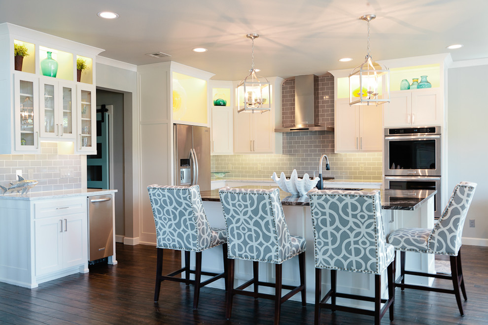 Inspiration for a mid-sized coastal u-shaped dark wood floor eat-in kitchen remodel with an undermount sink, shaker cabinets, white cabinets, granite countertops, gray backsplash, glass tile backsplash, stainless steel appliances and an island