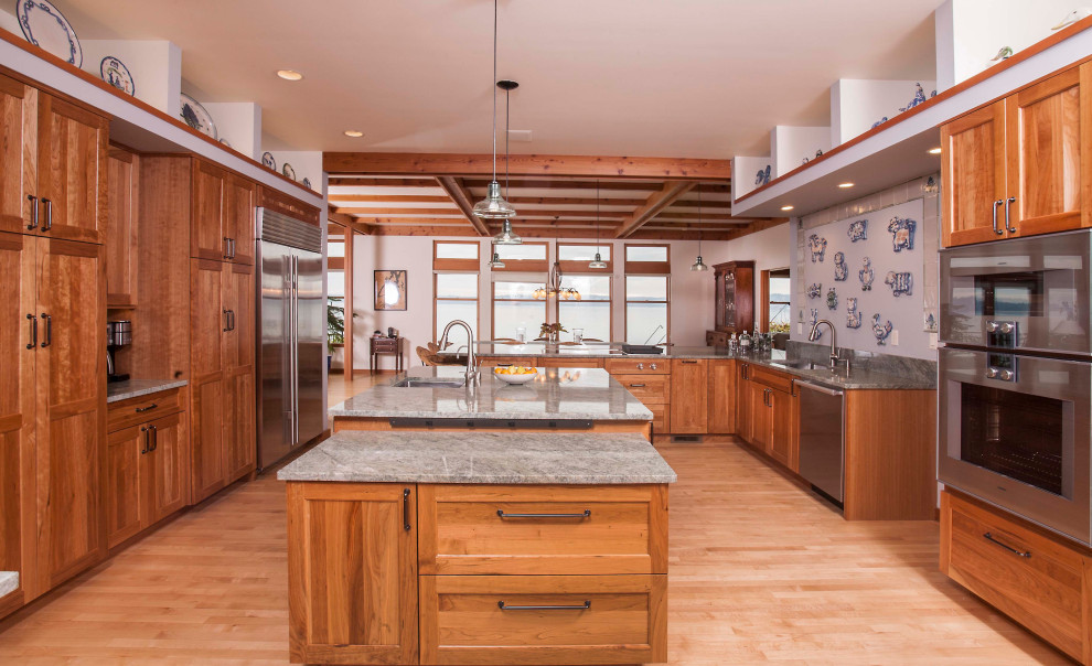 Photo of a large bohemian u-shaped kitchen/diner in Seattle with a submerged sink, raised-panel cabinets, medium wood cabinets, granite worktops, granite splashback, stainless steel appliances, an island, green worktops, exposed beams, green splashback, light hardwood flooring and brown floors.