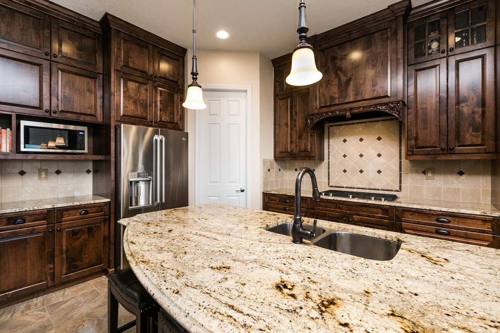 This is an example of a large l-shaped kitchen/diner in Albuquerque with a submerged sink, raised-panel cabinets, dark wood cabinets, granite worktops, beige splashback, ceramic splashback, stainless steel appliances, porcelain flooring, an island and brown floors.