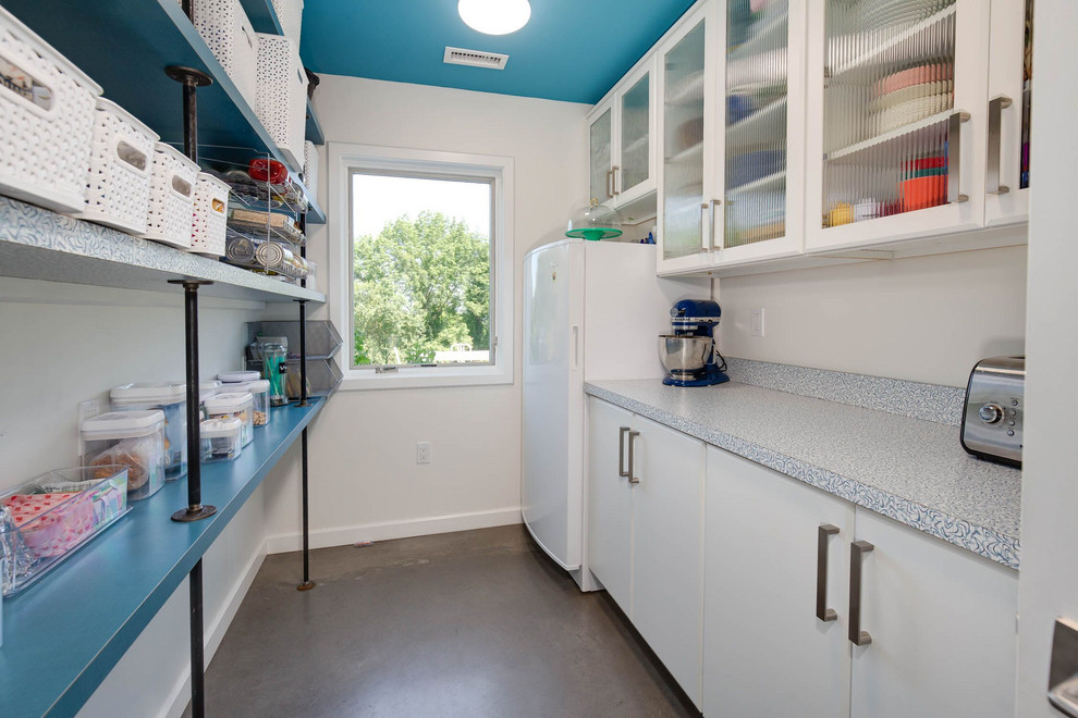 This is an example of a mid-sized industrial galley kitchen pantry in Bridgeport with flat-panel cabinets, white cabinets, laminate benchtops, multi-coloured splashback, white appliances, concrete floors, grey floor and blue benchtop.