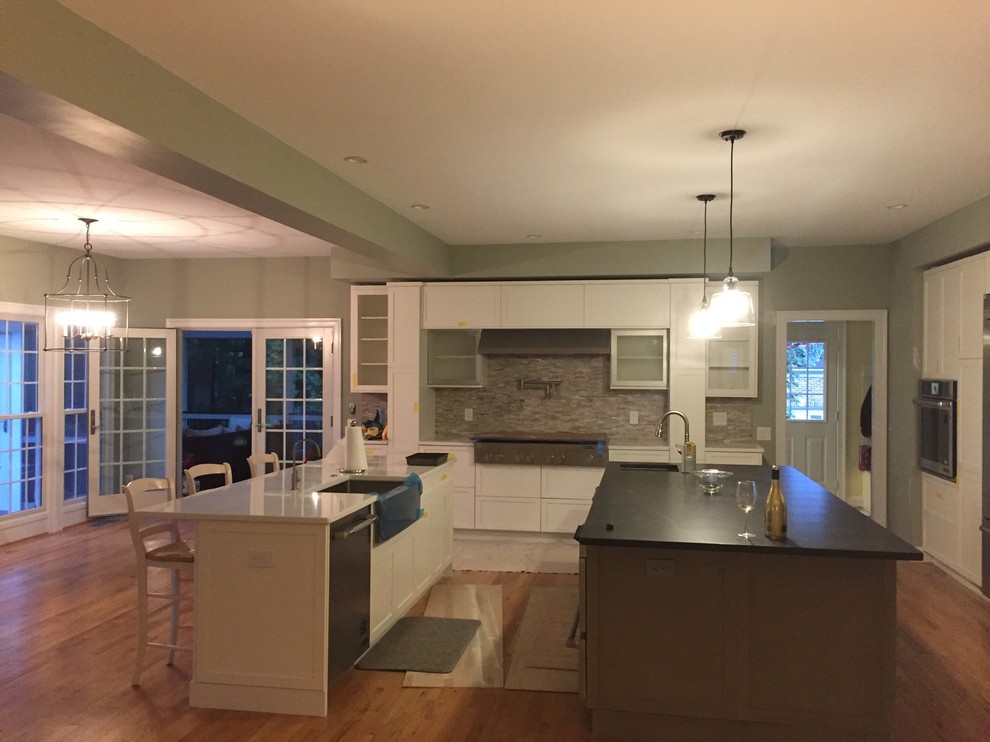 Inspiration for a large transitional single-wall medium tone wood floor and brown floor open concept kitchen remodel in DC Metro with a farmhouse sink, recessed-panel cabinets, white cabinets, gray backsplash, ceramic backsplash, stainless steel appliances, two islands and white countertops