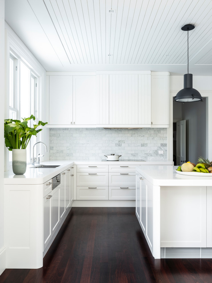 Exempel på ett modernt vit vitt kök med öppen planlösning, med en undermonterad diskho, skåp i shakerstil, vita skåp, bänkskiva i koppar, grått stänkskydd, stänkskydd i marmor, integrerade vitvaror, mörkt trägolv, en köksö och brunt golv