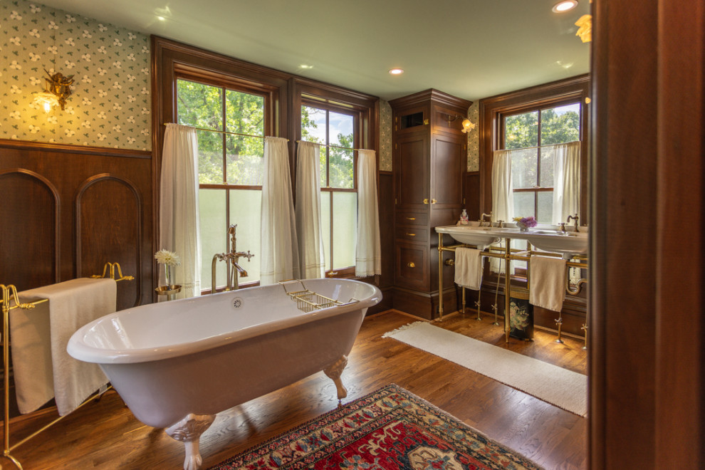 This is an example of a large traditional master bathroom in Cincinnati with furniture-like cabinets, brown cabinets, a claw-foot tub, a corner shower, a one-piece toilet, dark hardwood floors, a pedestal sink, granite benchtops, brown floor, a hinged shower door, white benchtops, an enclosed toilet, a double vanity, a freestanding vanity and decorative wall panelling.