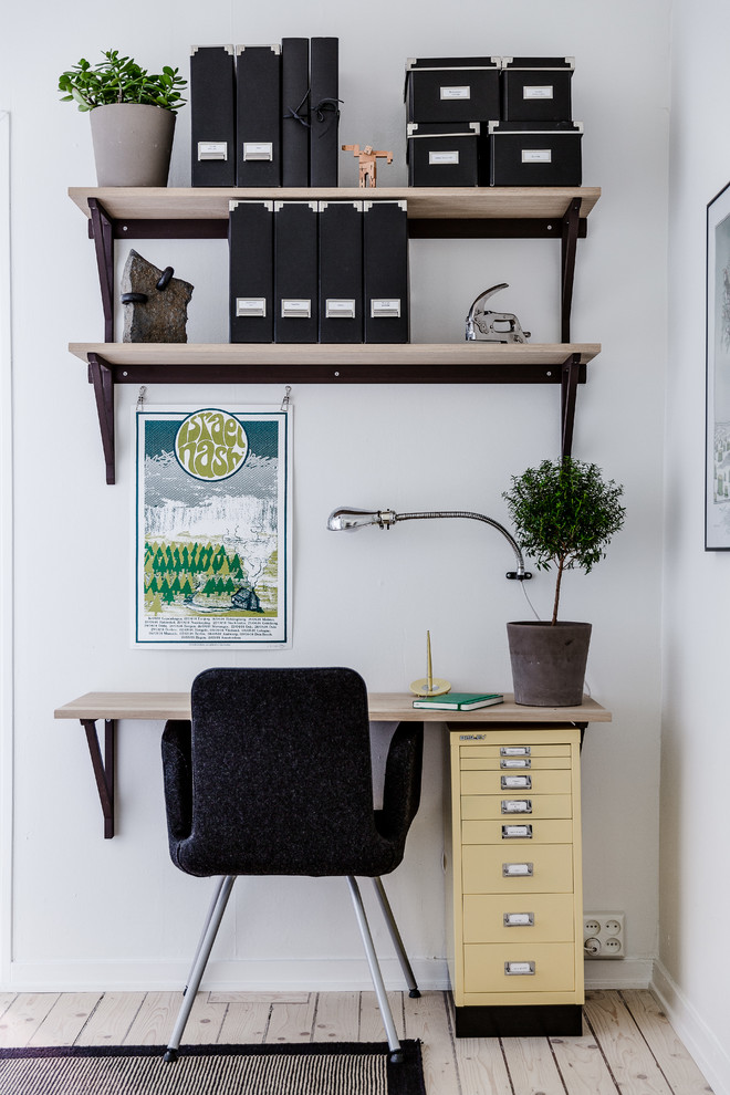 Photo of a small scandinavian home office in Gothenburg with white walls, light hardwood floors and a built-in desk.