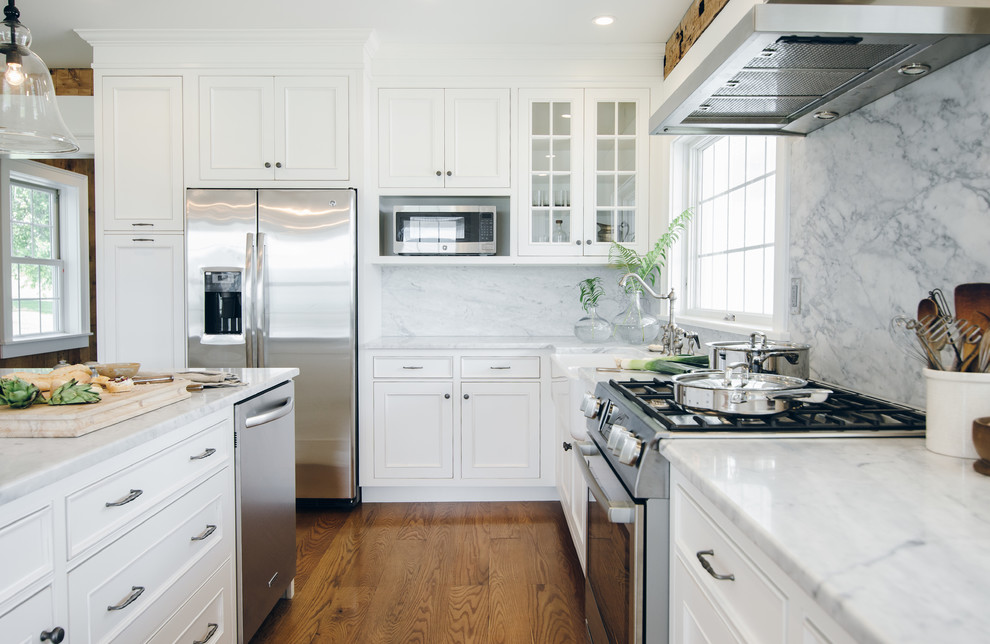 Photo of a large country u-shaped eat-in kitchen in New York with a farmhouse sink, beaded inset cabinets, white cabinets, marble benchtops, white splashback, stone slab splashback, stainless steel appliances, medium hardwood floors and with island.
